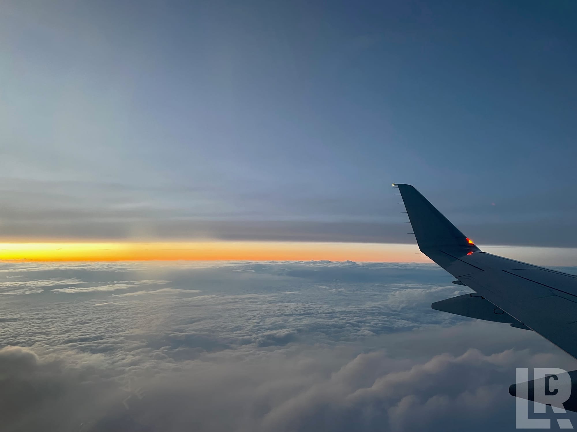 Airplane wing over clouds at sunrise with orange and yellow horizon