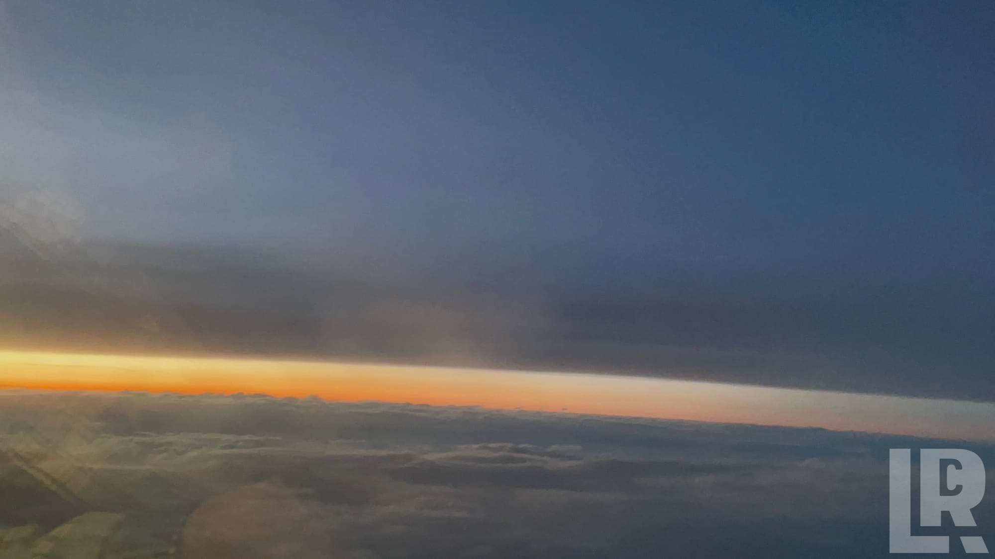 Aerial view of a sunset horizon with orange glow between clouds and dark blue sky