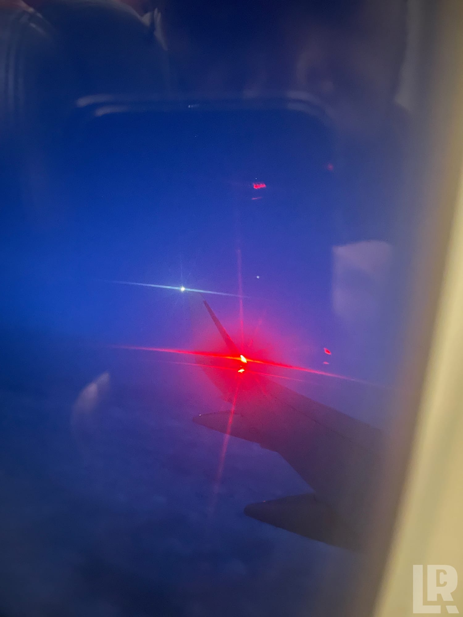 Bright red aircraft wing navigation light seen through airplane window at night