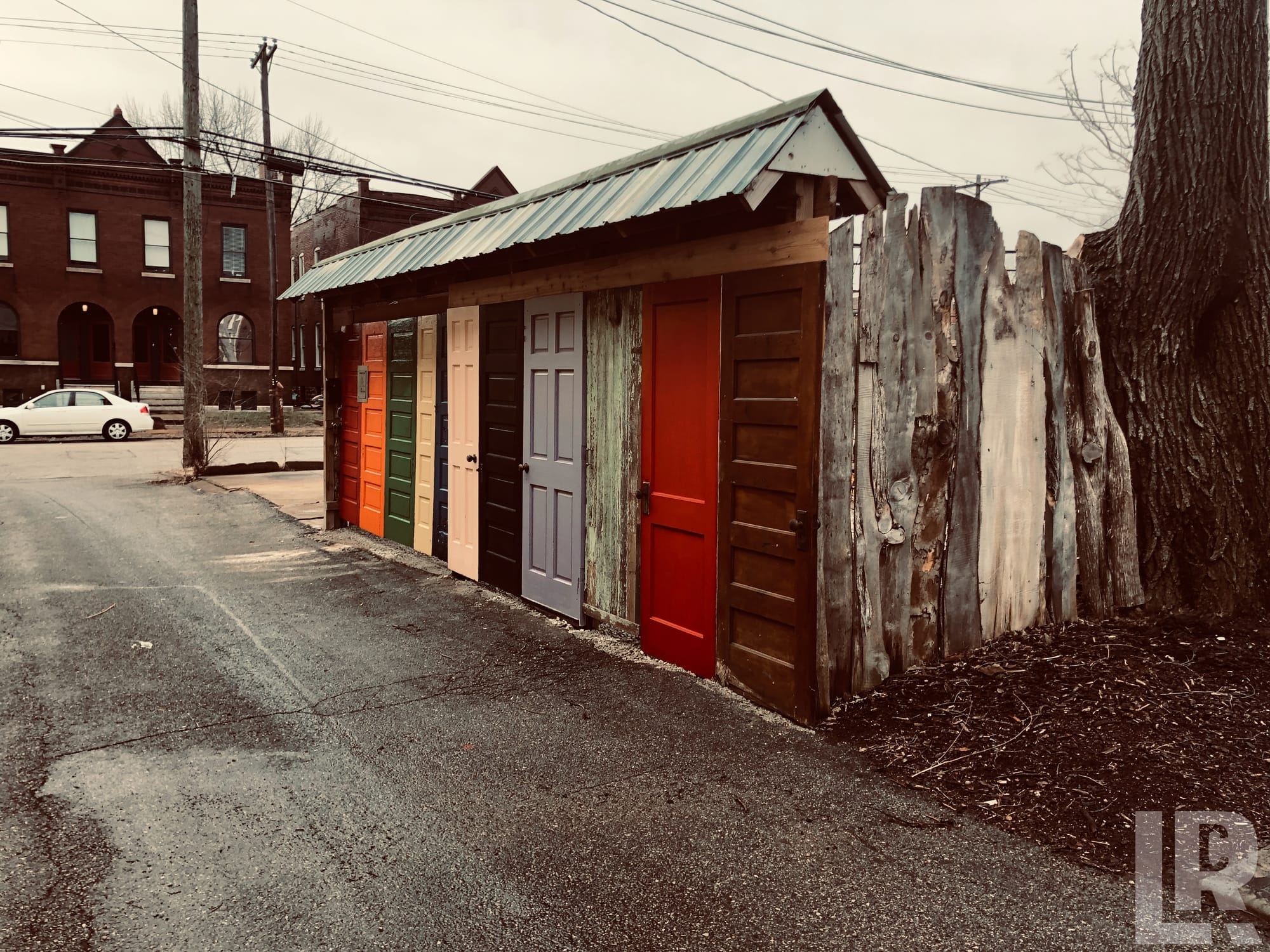 Small shed made from colorful salvaged doors with a metal roof on an urban street corner