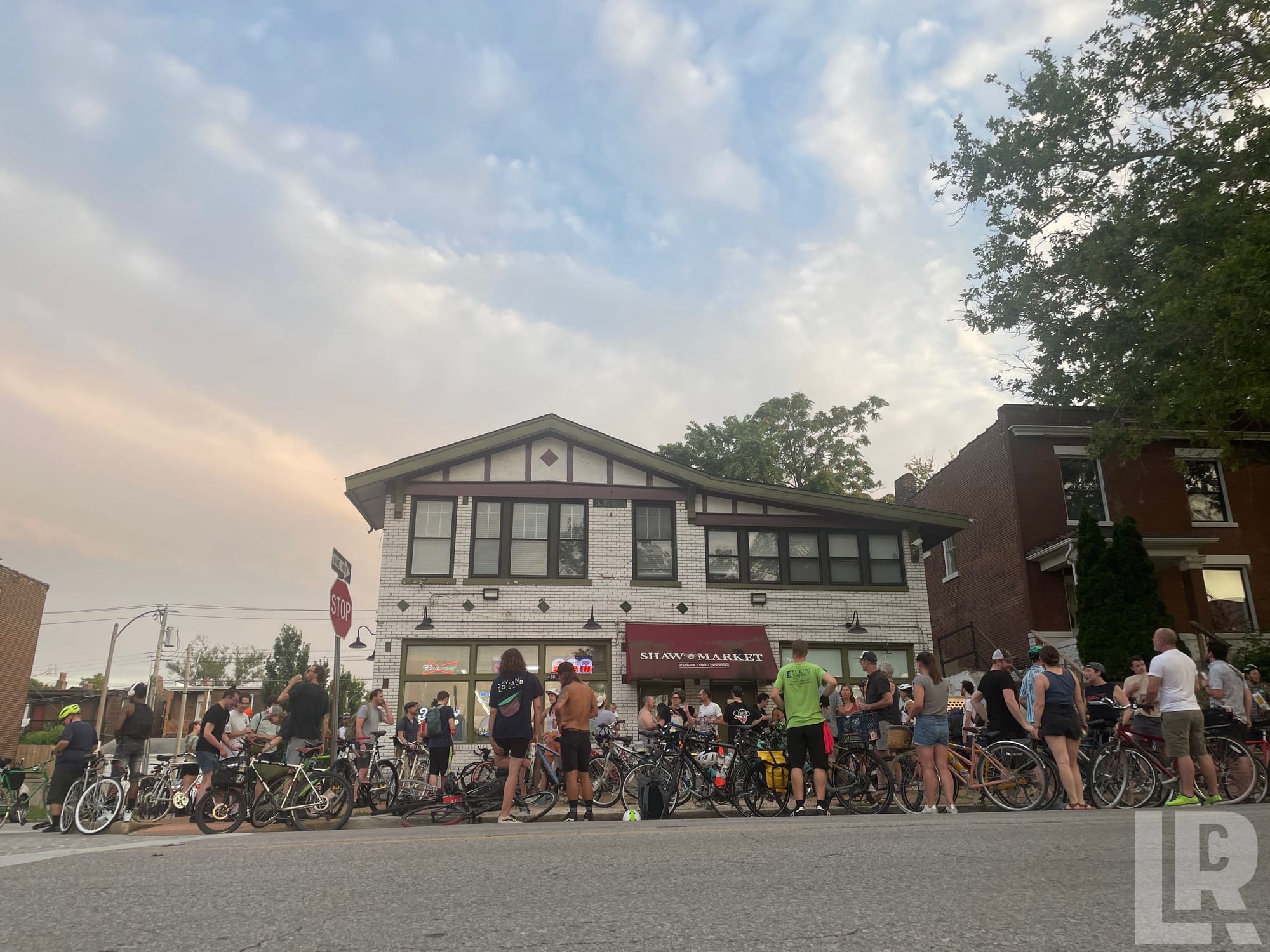 Crowd of cyclists gathered in front of Shaw Market at dusk