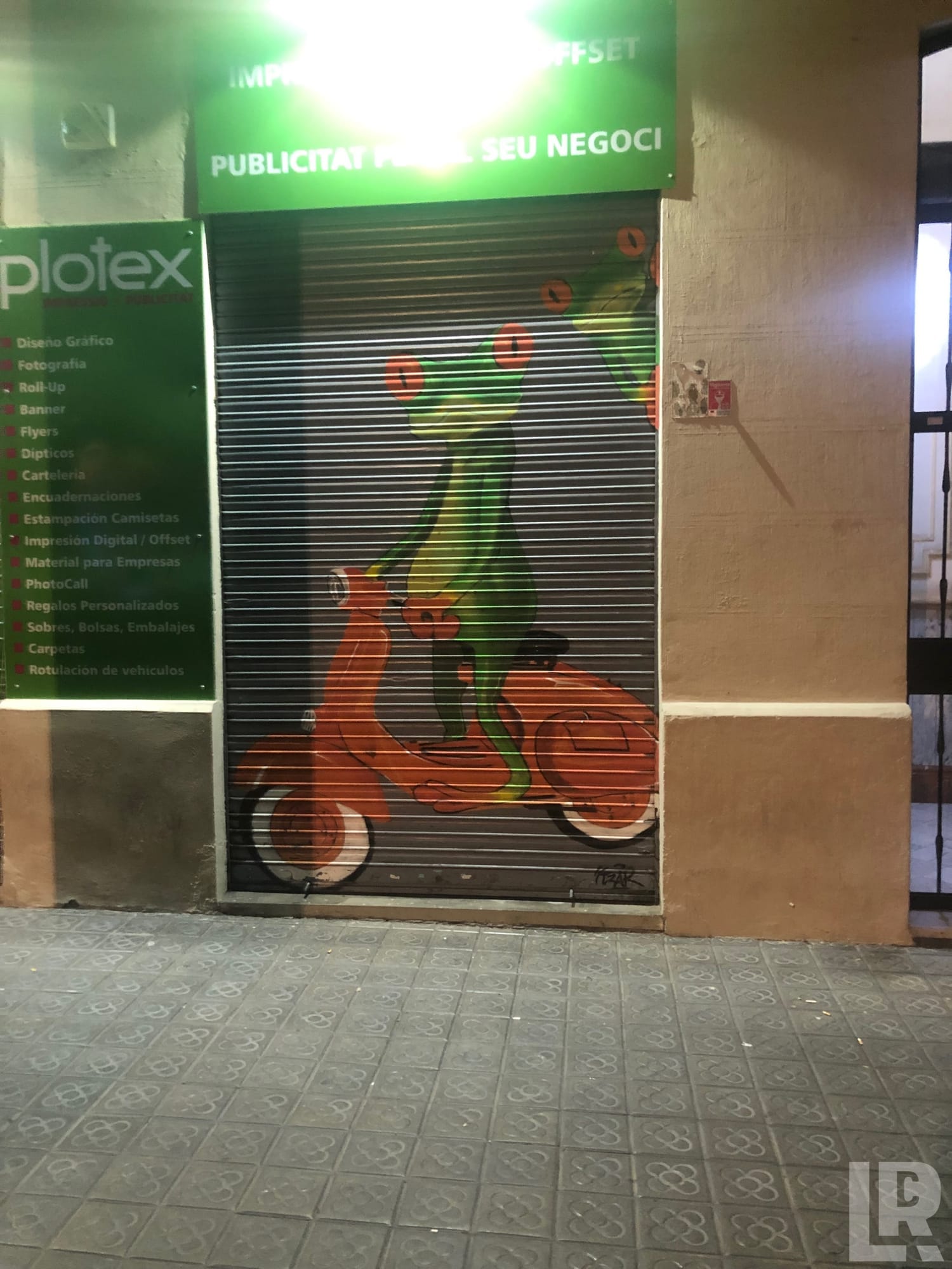 Graffiti mural of a person on an orange scooter painted on a closed shop shutter at night