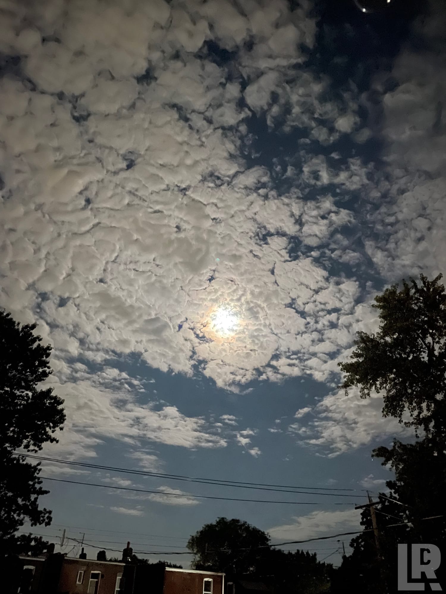 Full moon glowing through a thick layer of altocumulus clouds at night over a residential neighborhood