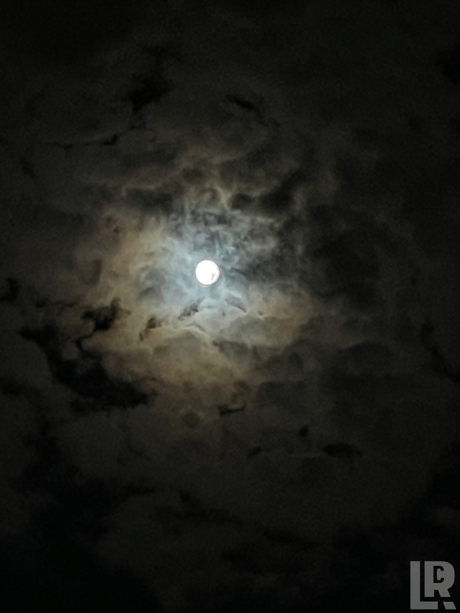 Full moon shining behind dramatic clouds at night