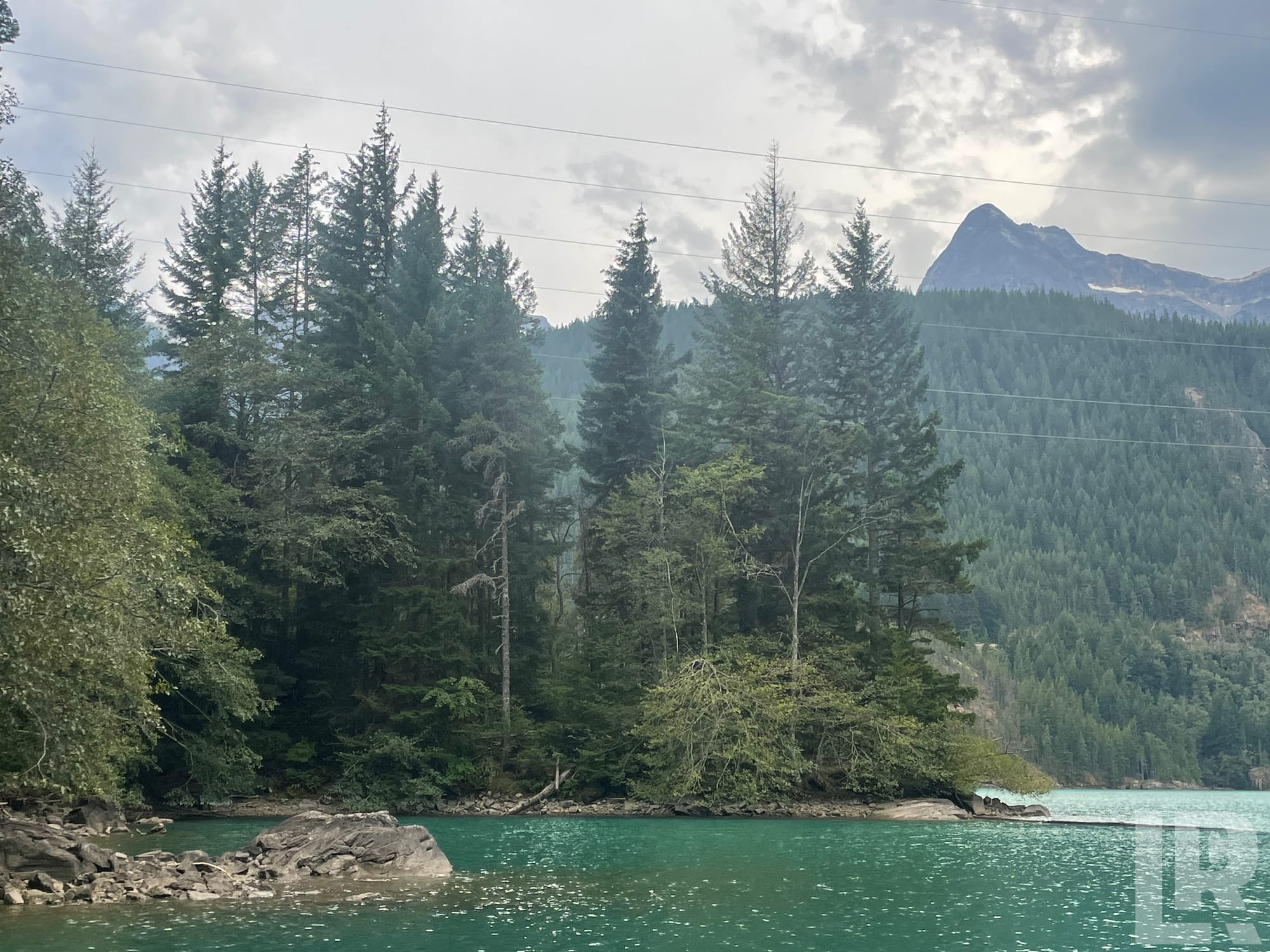 Turquoise lake with forested rocky shoreline and mountain peaks in the background