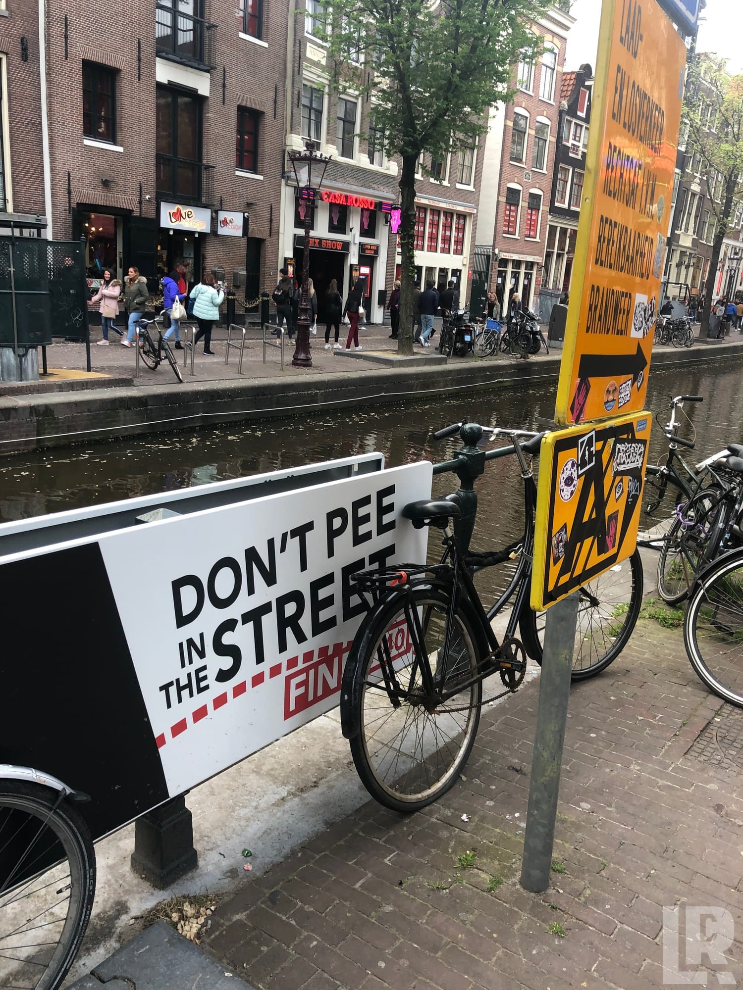 Don't pee in the street warning sign along a canal with bicycles and city buildings in background
