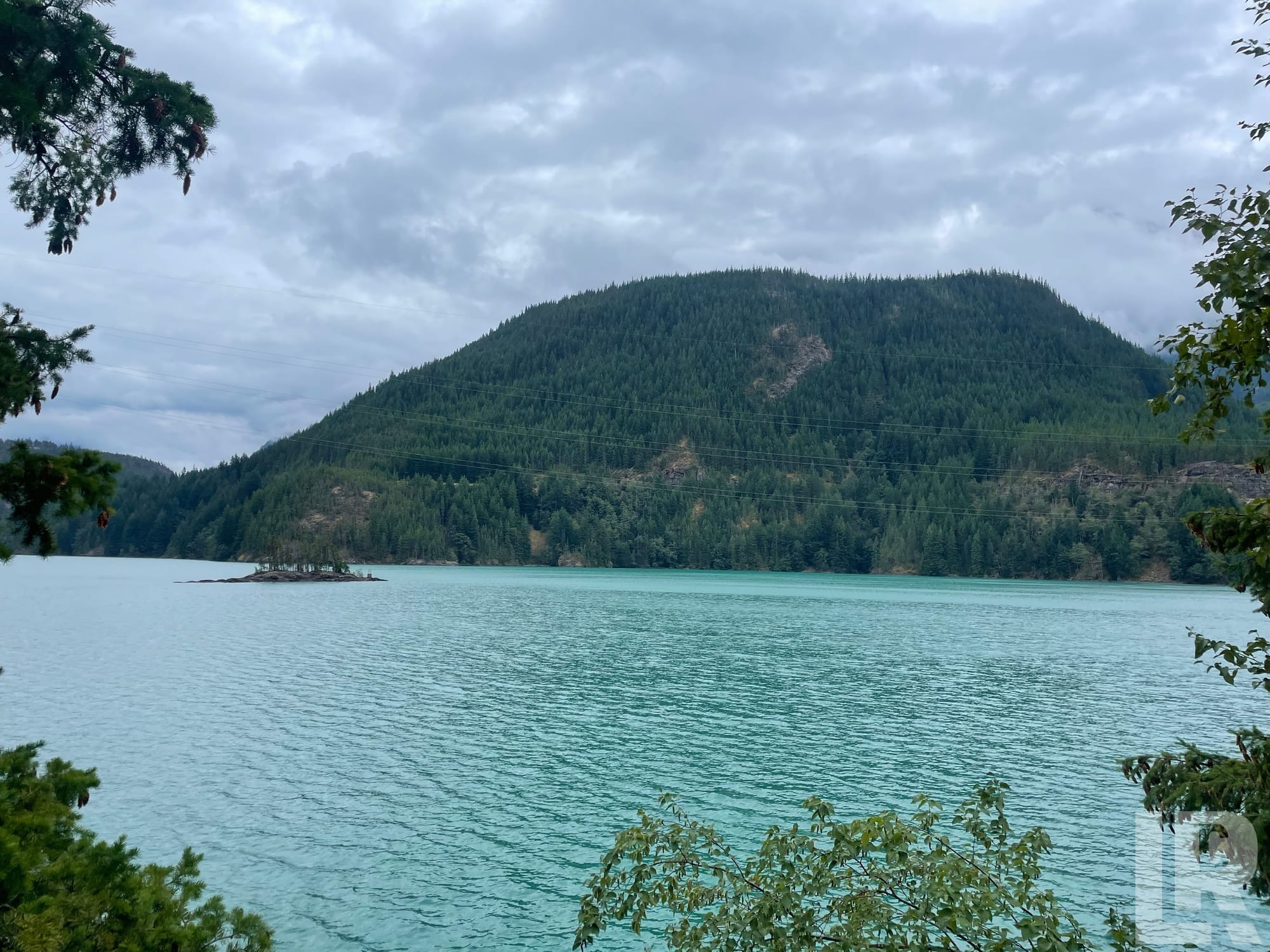 Turquoise lake with a forested mountain and overcast sky