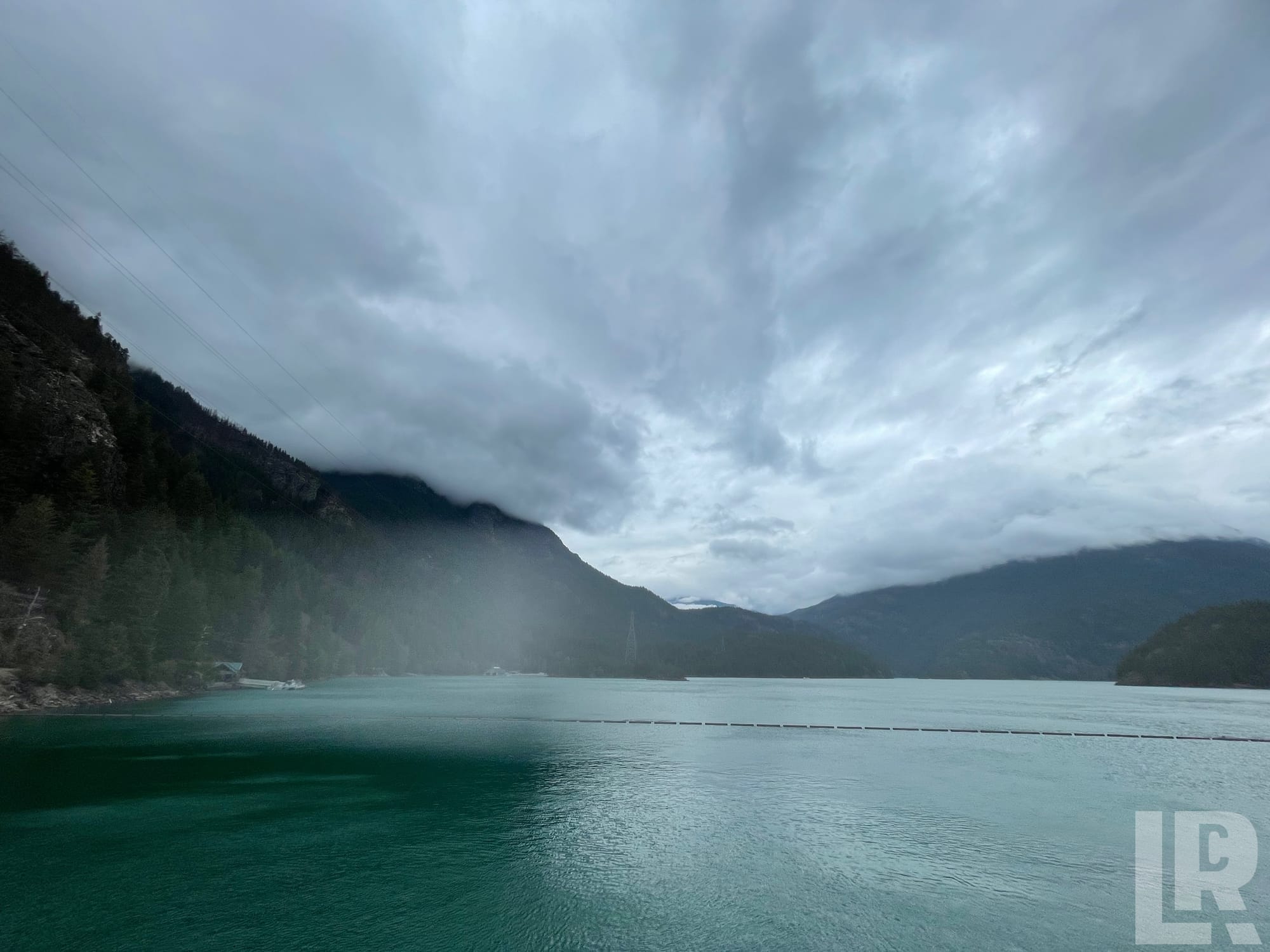 Turquoise mountain reservoir with misty forested peaks and cloudy sky