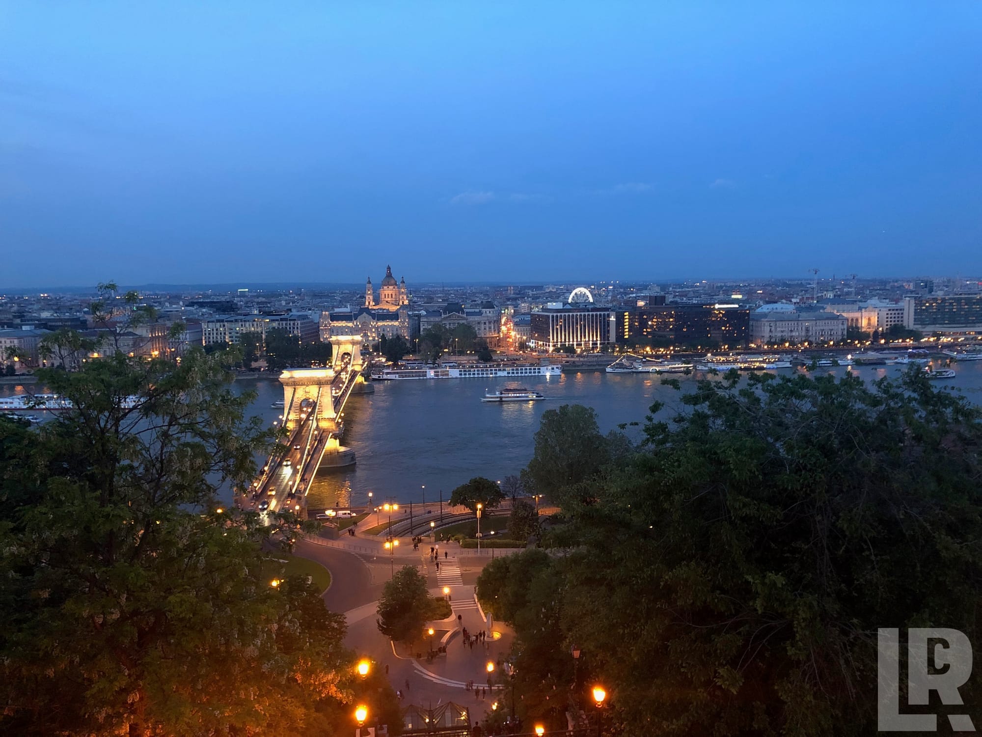 Illuminated suspension bridge over a river at dusk with city lights reflecting on the water