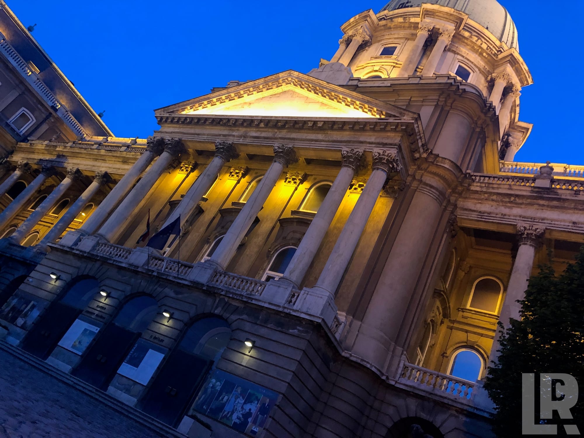 Looking up at a floodlit neoclassical building with Corinthian columns and a dome at dusk