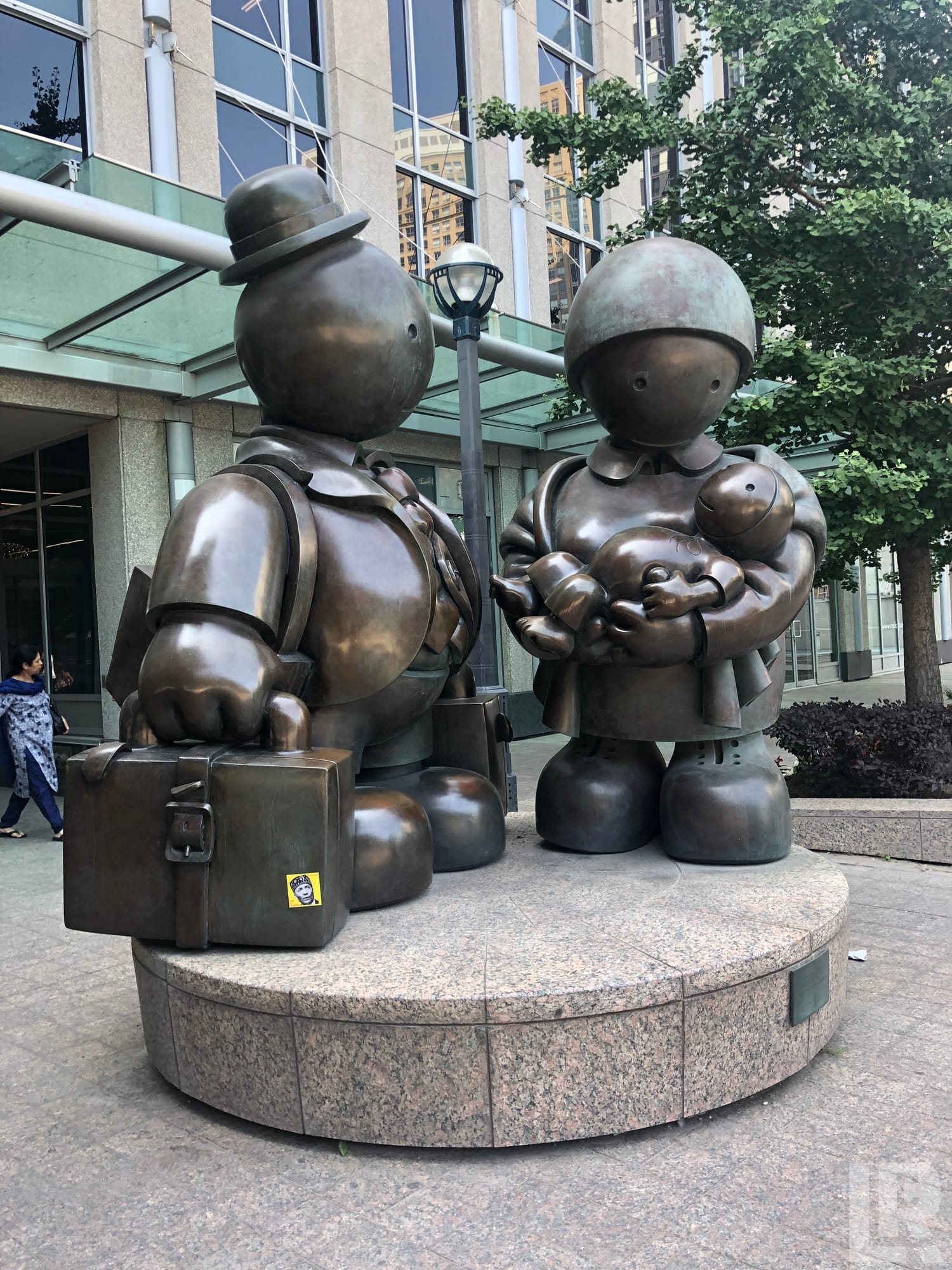 Large bronze sculptures of two rounded cartoon-style figures on a granite base in a city plaza