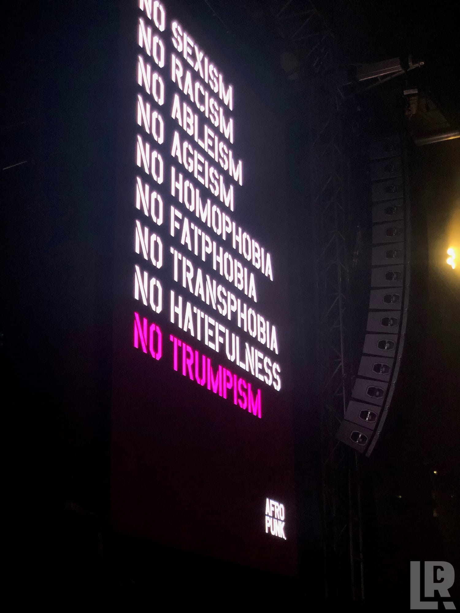 LED sign listing no sexism, racism, ableism, ageism, homophobia, fatphobia, transphobia, hatefulness, and no Trumpism in pink, at Afro Punk
