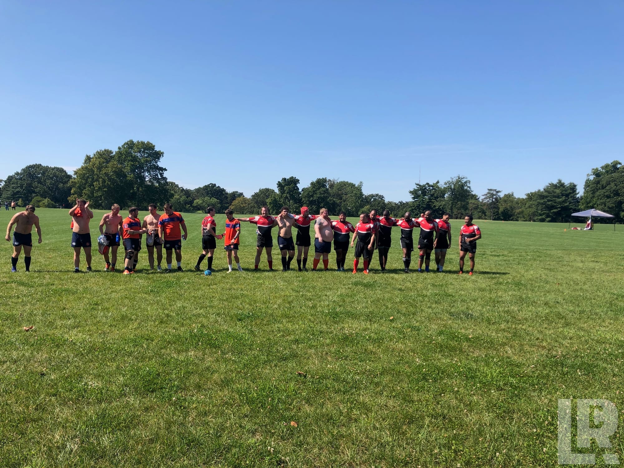 Rugby team posing in a line on a green field with trees in the background