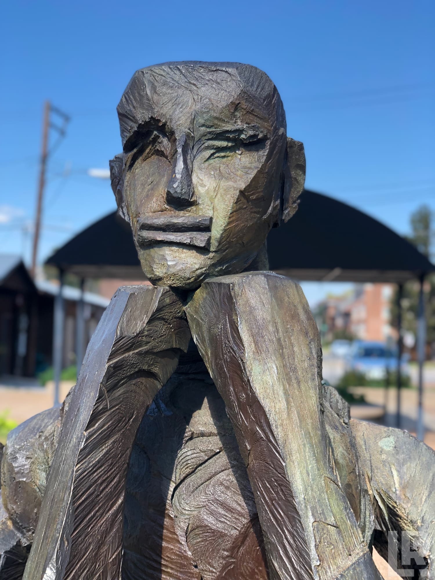 Bronze sculpture of a seated figure with hands raised near face, abstract expressionist style