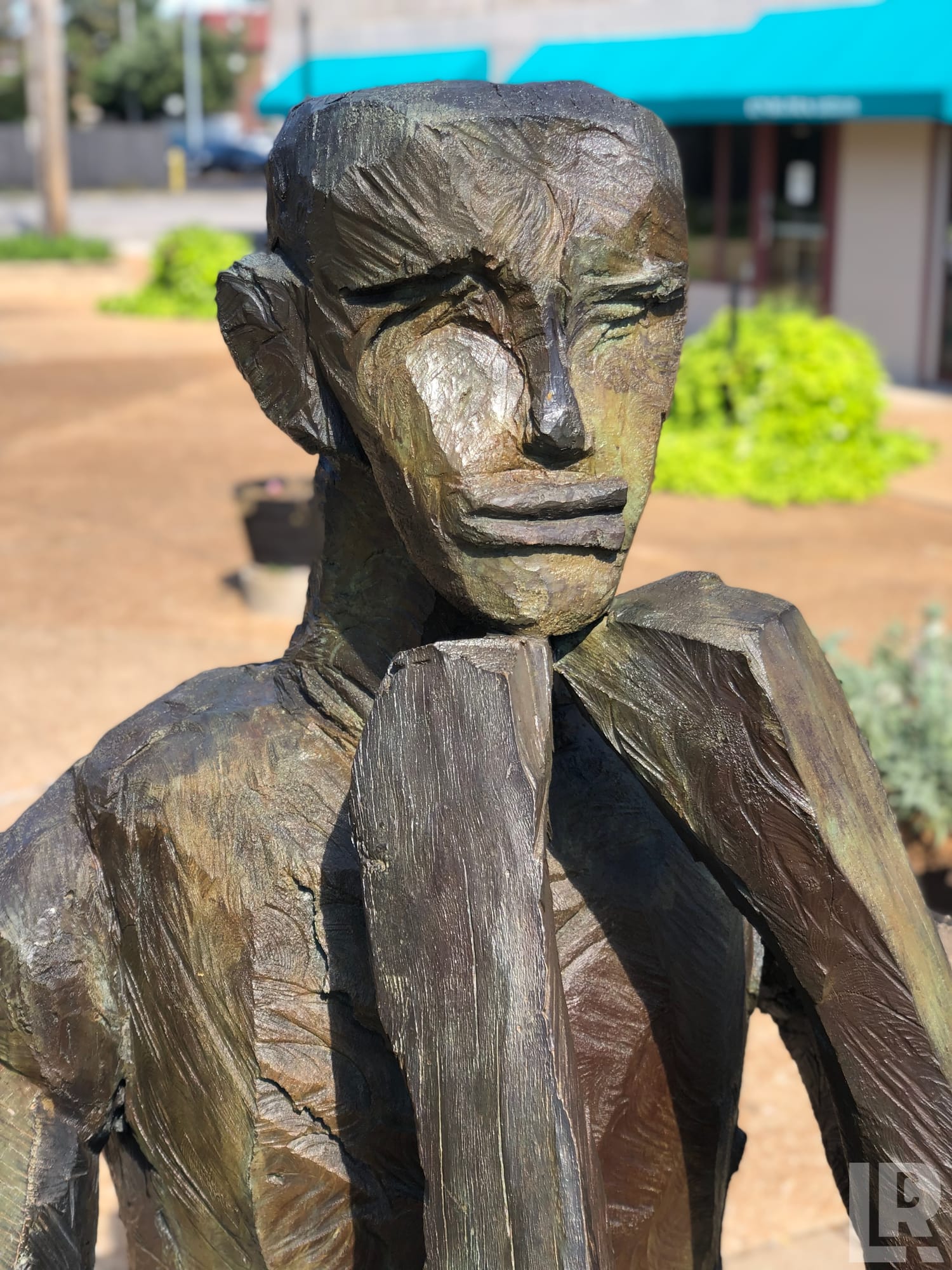 Bronze outdoor sculpture of a stylized human figure with angular features holding a post