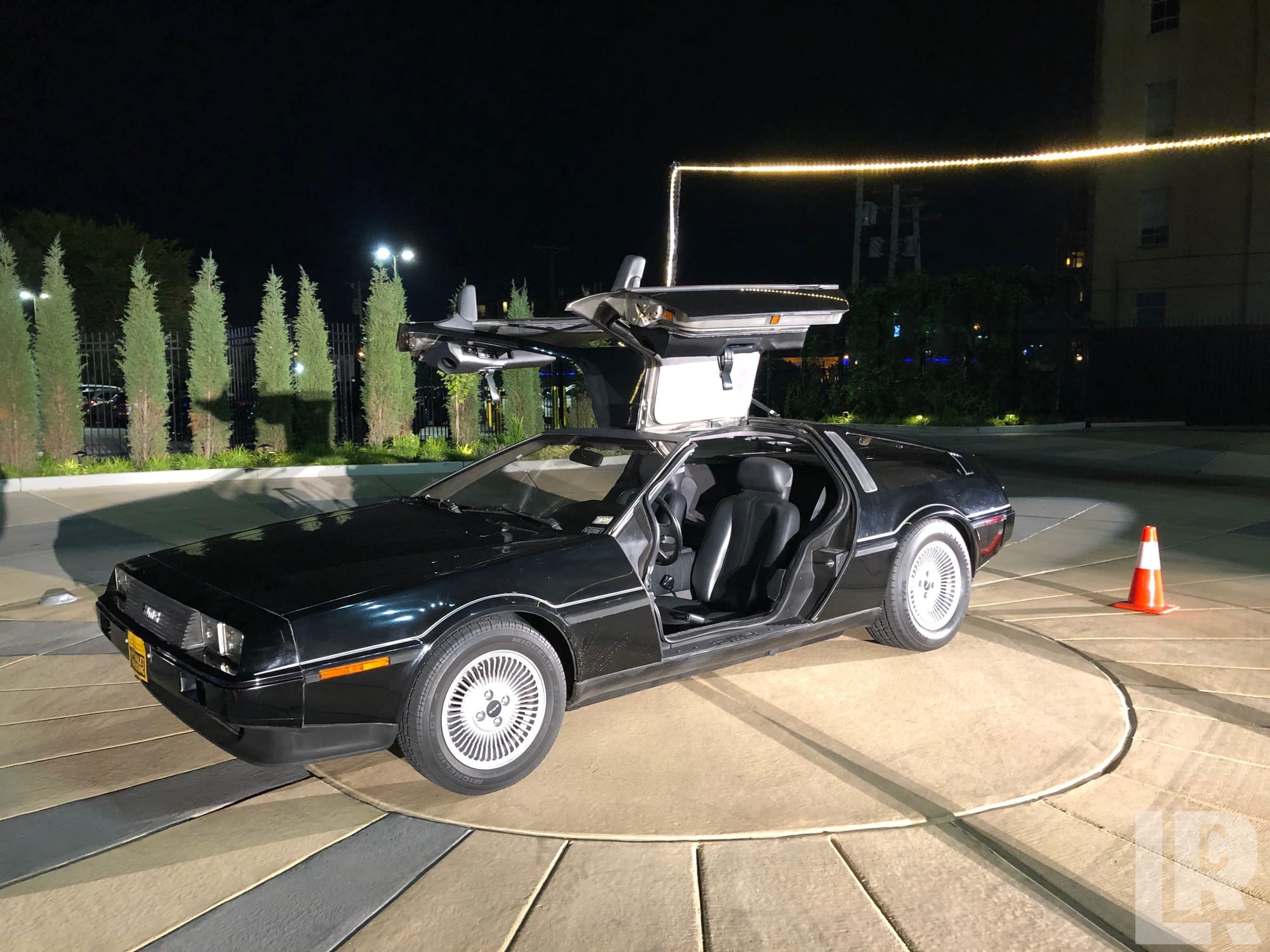 Black DeLorean DMC-12 with gull-wing doors open at night