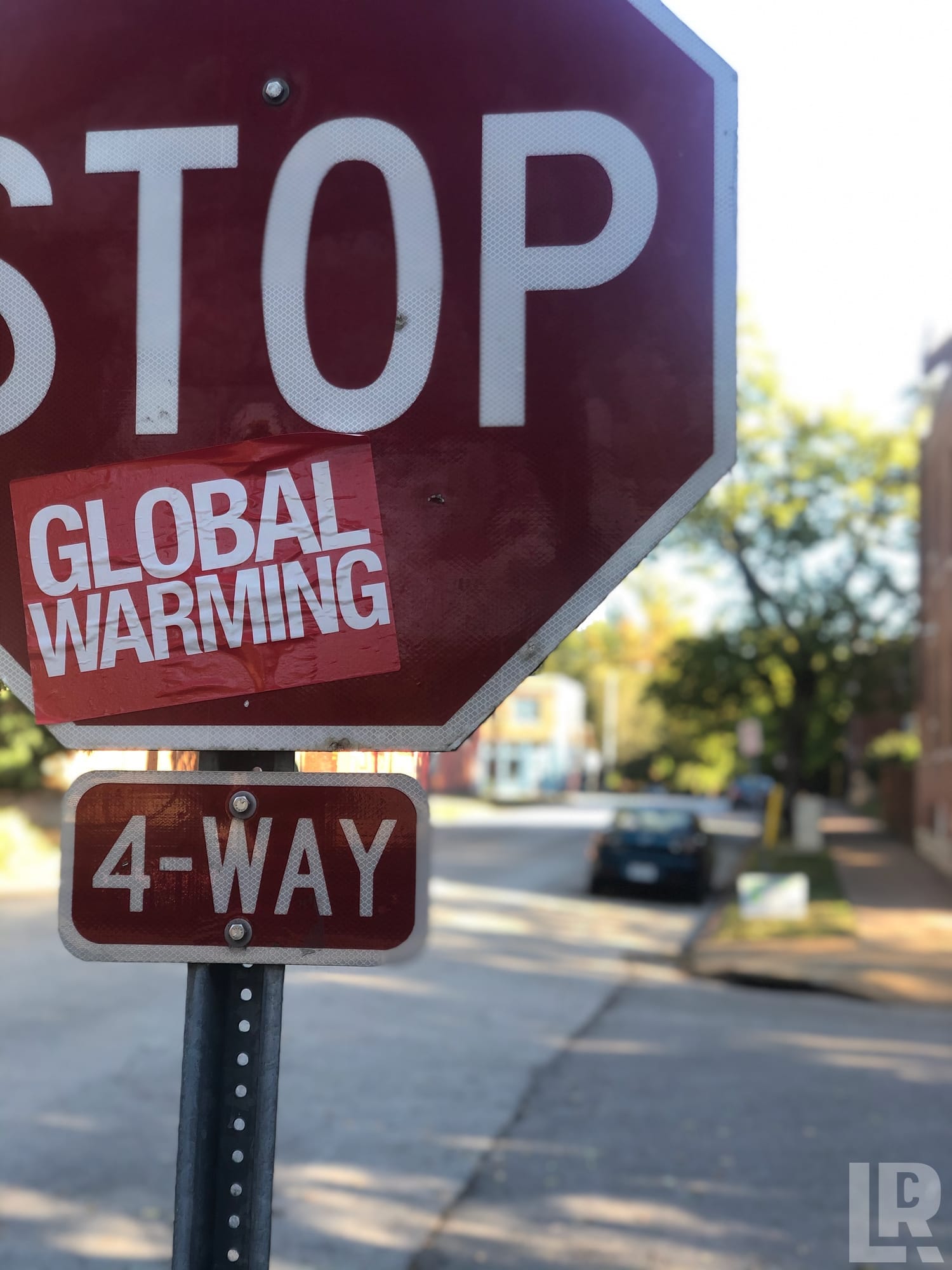 Stop sign with a Global Warming sticker forming the phrase Stop Global Warming at a 4-way intersection